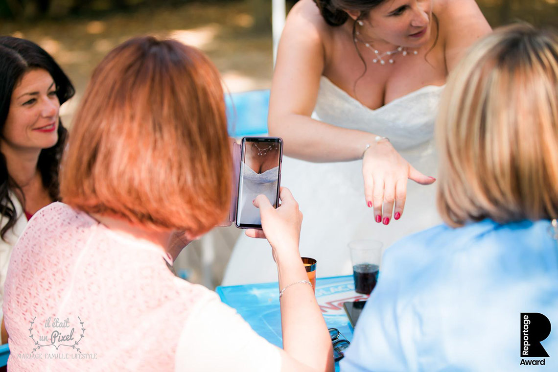 Photo de reportage de mariage rigolote ou une invitée photographie le décoleté de la mariée
