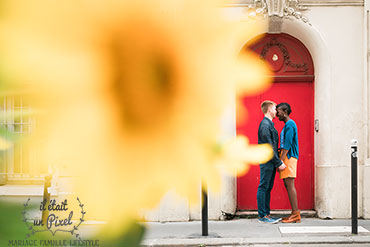 Couple face à face devant une porte rouge à Paris avec une fleur en premier plan