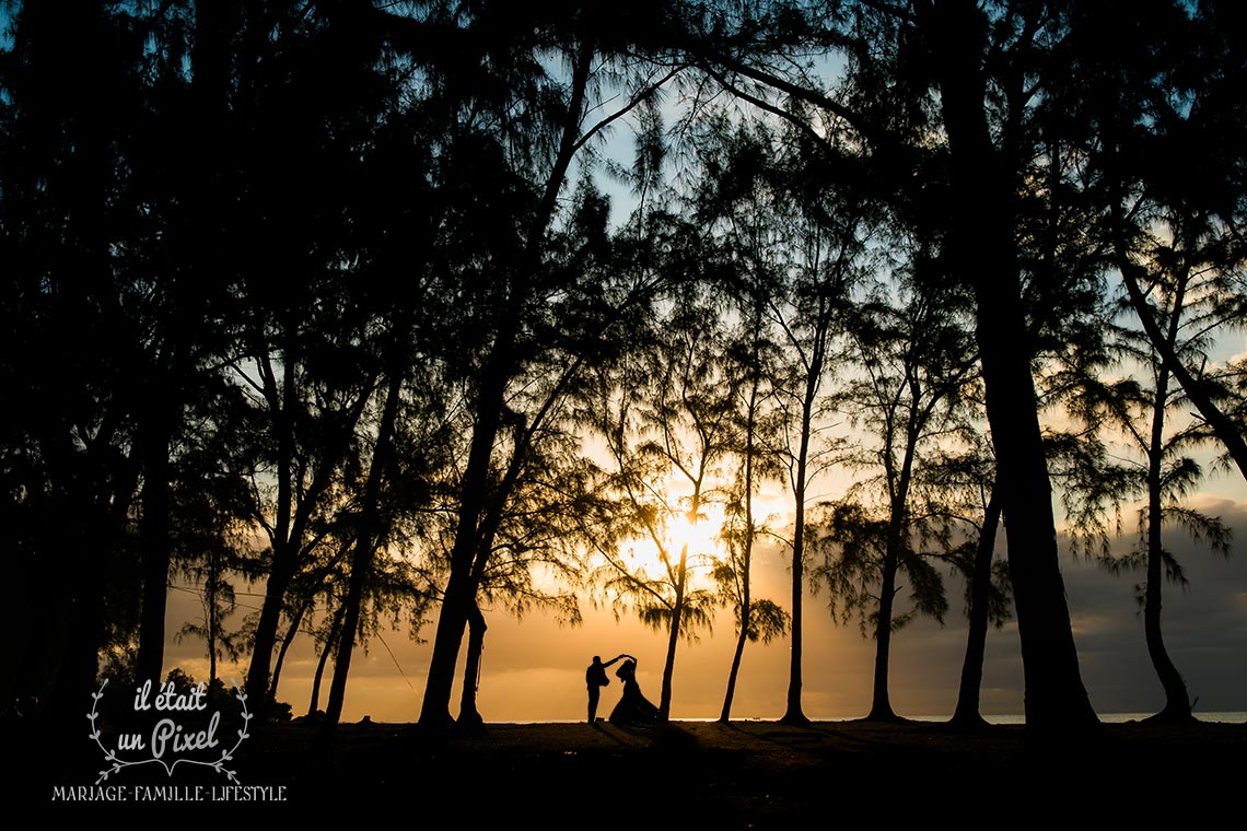 Photo de silhouette d'un couple de mariés au coucher du soleil dansant au milieu des arcbre filao sur une plage de l'ile Maurice