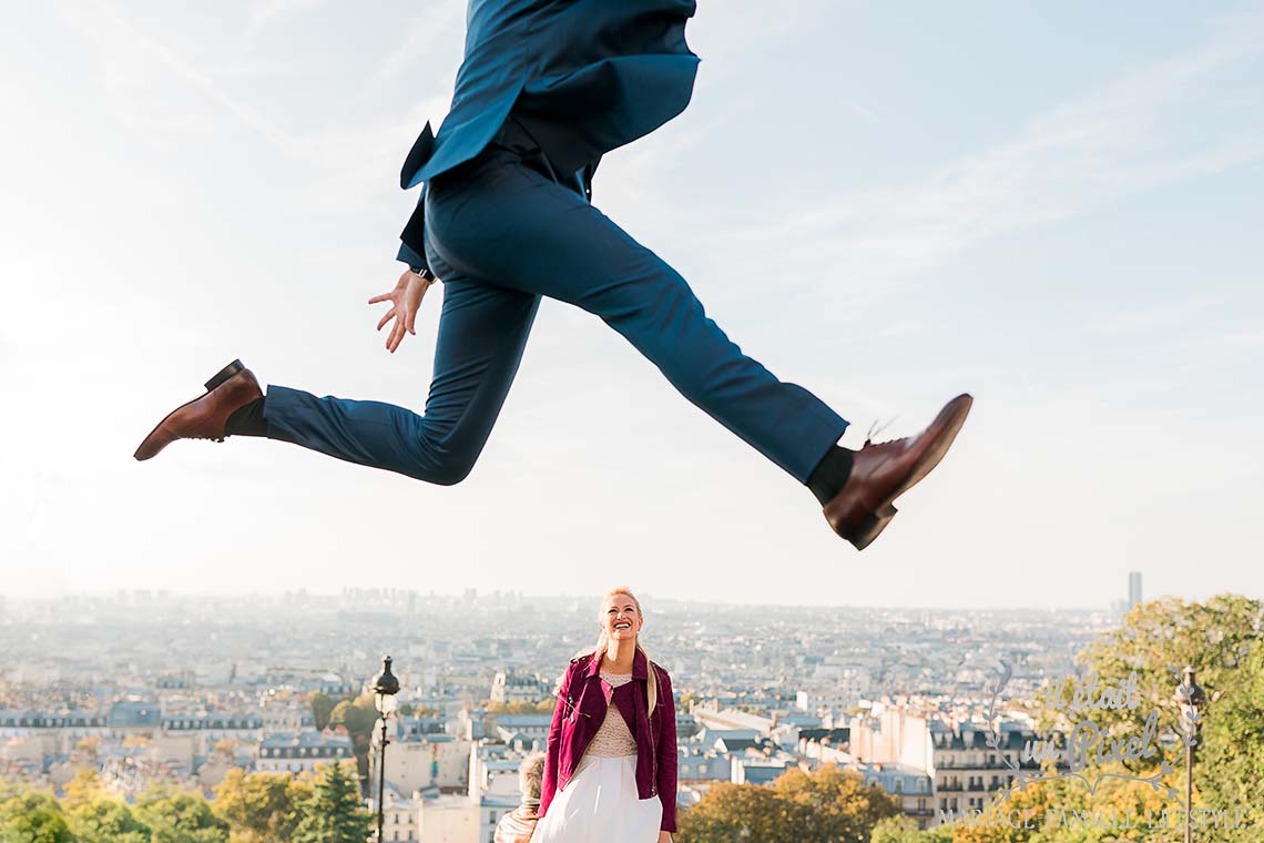 Mariée rock n roll riant pendant que son mari saute devant elle en haut des marches de Montmartre pendant leur shooting day after à Paris