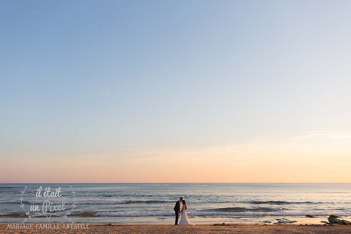Couple de marié s'embrassant sur la plage au coucher du soleil avec beaucoup d'espace négatif et un ciel coloré