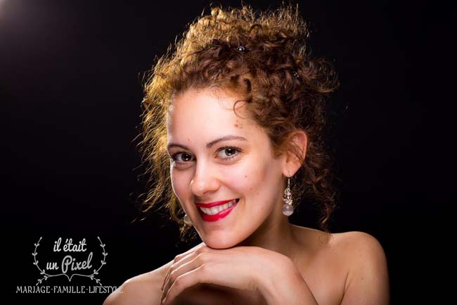 Portrait studio sur fond noir d'une jeune femme avec rouge à levres pendant un shooting photo beauté