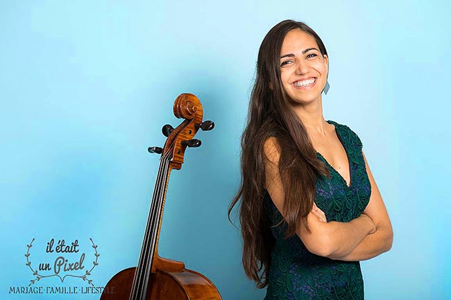 Protrait en studio de la violoncelliste internationale Juliette Salmona avec son instrument sur fond bleu clair pendant un shooting photo