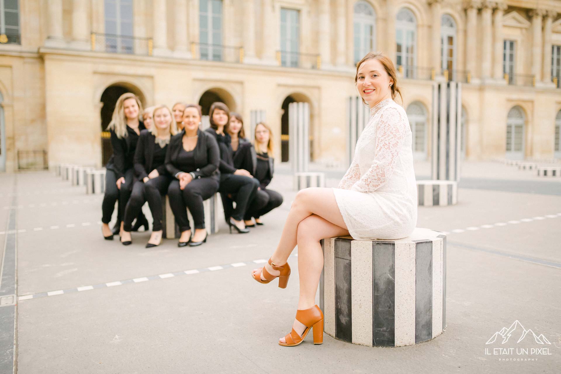 Photo de groupe lors d'un shooting EVJF au Palais Royal à Paris avec les participantes toutes regroupées en arriere plan et la future mariée assise au premier plan