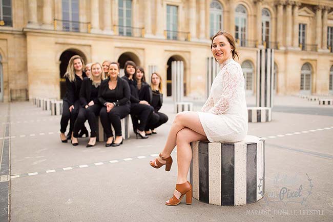Photo de groupe lors d'un shooting EVJF au Palais Royal à Paris avec les participantes toutes regroupées en arriere plan et la future mariée assise au premier plan