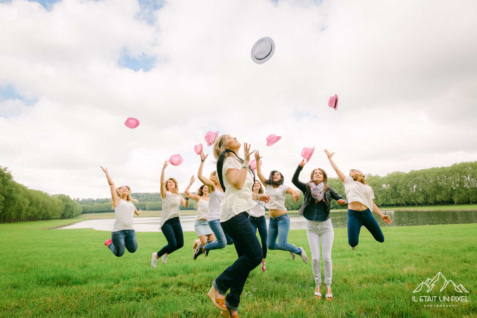 Photo de groupe lors d'un shooting EVJF à Versailles avec les participantes sautant et jetant leur chapeaux roses en l'air