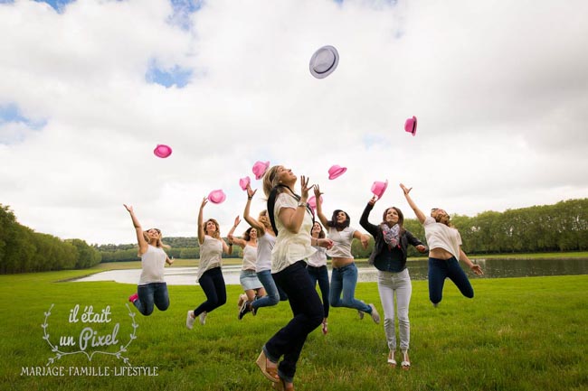 Photo de groupe lors d'un shooting EVJF à Versailles avec les participantes sautant et jetant leur chapeaux roses en l'air