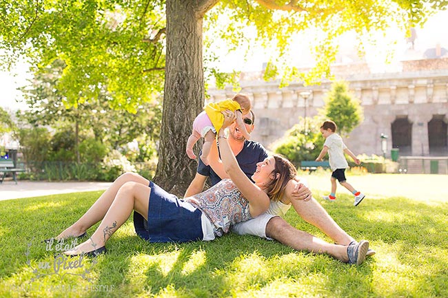 Photo de famille lifestyle au square du vert galant à Paris avec un bébé en l'air dans les bras et son frere courant autour d'eux 