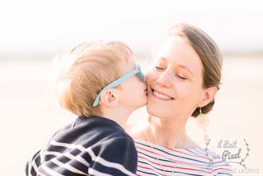 Young boy kissing his smiling mom on the chick on the beach at sunrise during a photo session