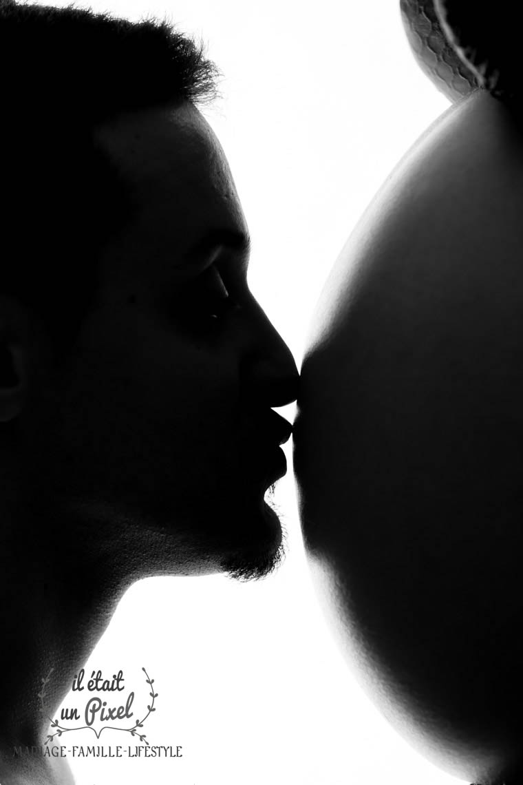 Visage d'un futur papa embrassant le ventre enceinte de sa femme lors d'un shooting grossesse en studio
