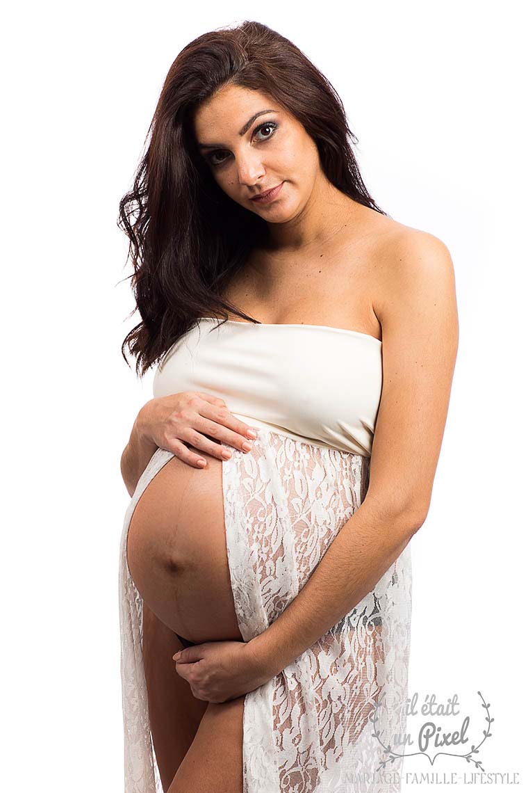 Future maman enceinte avec robe en dentelle blanche ouverte sur le ventre lors d'un shooting grossesse en studio
