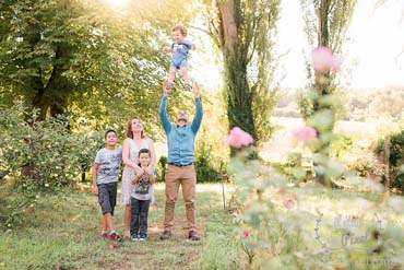 Photo de famille lifestyle dans leur jardin avec le papa jetant un de ses fils en l'air 