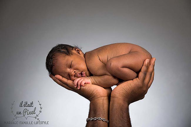 Photo d'un bébé dans les mains de son pere lors d'un shooting naissance type newborn posing en studio