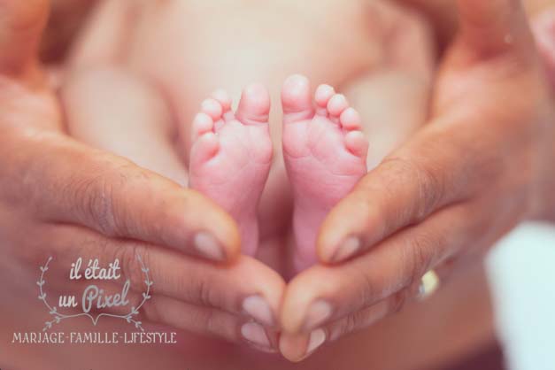 Photo des pieds d'un bébé dans les mains de son papa lors d'un shooting naissance 