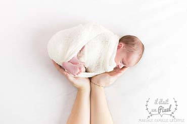 Photo d'un bébé enveloppé avec les mains de sa maman lors d'un shooting naissance type newborn posing en studio
