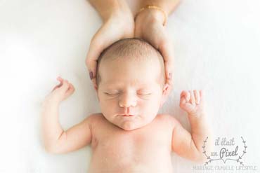 Photo du visage d'un bébé dans les mains de sa maman lors d'un shooting naissance en studio