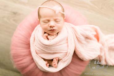 Photo d'un bébé enveloppé et sur un nid rose lors d'un shooting naissance type newborn posing a domicile