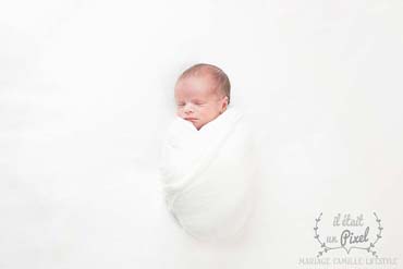Photo d'un bébé enveloppé  en blanc lors d'un shooting naissance type newborn posing en studio