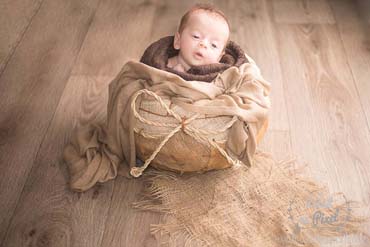 Photo d'un bébé dans un bol coco lors d'un shooting naissance a domicile