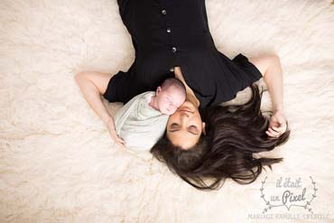 Photo d'un bébé enveloppé avec sa maman sur flokati lors d'un shooting naissance type newborn posing en studio
