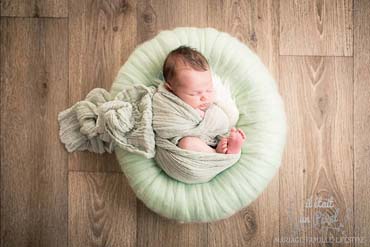 Photo d'un bébé enveloppé et sur un nid lors d'un shooting naissance type newborn posing en studio