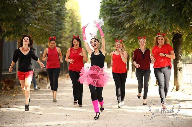 Photo de groupe lors d'un shooting EVJF aux Tuileries à Paris avec les participantes déguisées en diablesses courant derriere la future mariée portant une jupe en tule rose