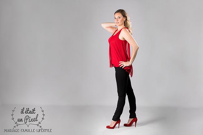 Portrait en pied sur fond clair d'une jeune femme avec haut rouge et talons rouges pendant un shooting en studio