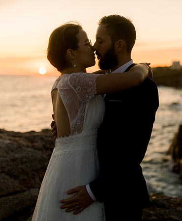 Couple de mariés s'enlancant au coucher du soleil sur les rochers au dessus de la mer aux Sables d'Olonne pendant un shooting day after