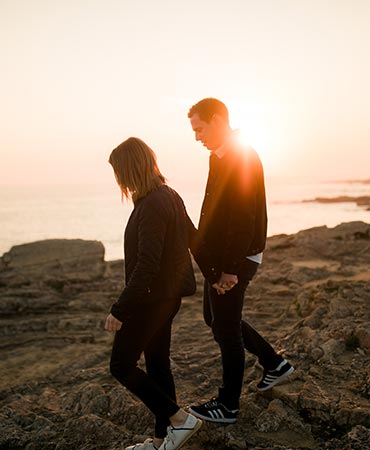 Couple marchant au coucher du soleil sur les rochers au dessus de la mer en Vendée pendant une seance engagement