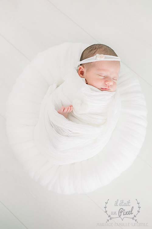 Photo de bébé en studio type newborn posing avec nouveau né dans un nid en laine blanc
